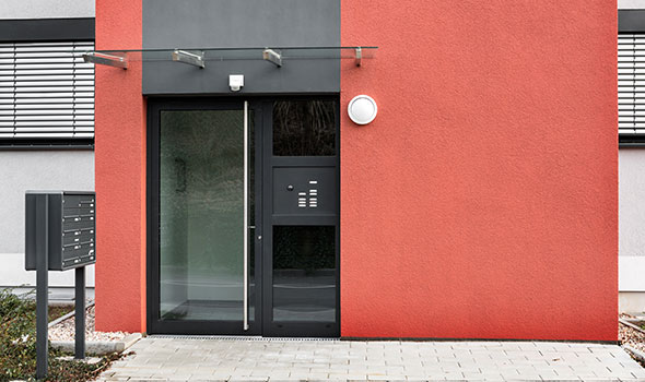 Rote Hausfassade mit einer Haustür in Anthrazit, passende Klingelanlage und freistehende Briefkästen